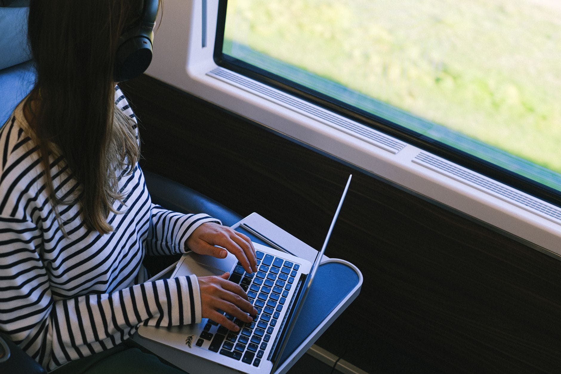 Osoba w słuchawkach pracuje na laptopie w pociągu podczas podróży